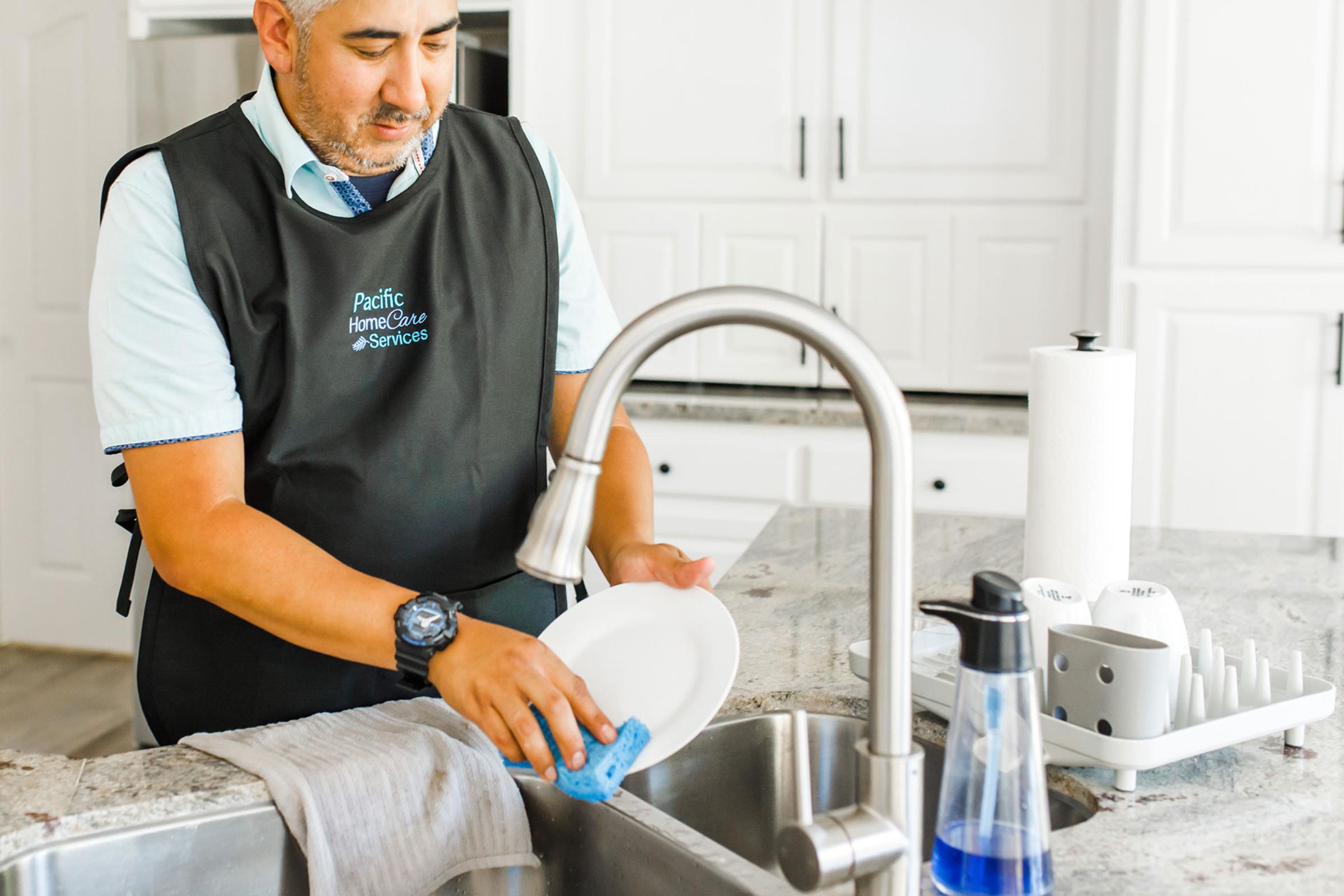 Male care provider washing dishes in sink